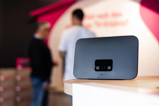 WLAN-Router auf Tresen in Telekom-Shop, unscharfe Personen im Hintergrund, moderne Technik.