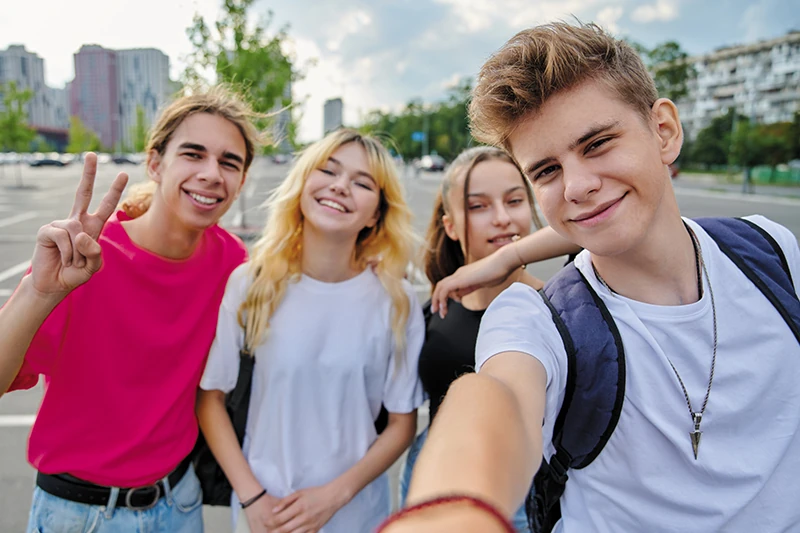 Vier Jugendliche machen ein Selfie draußen in der Stadt und lachen in die Kamera.